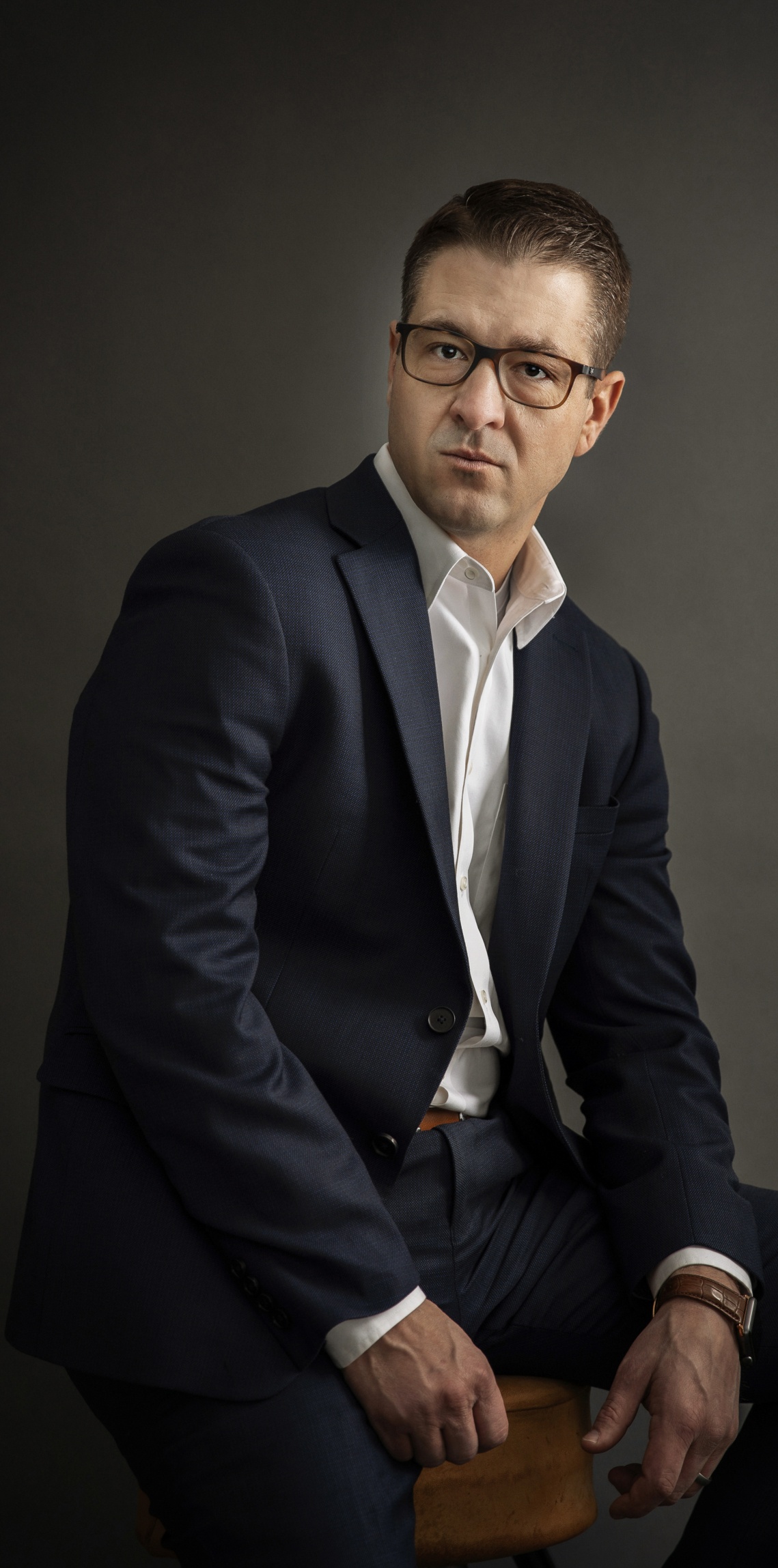 Professional image of C.J. Zwick, Esp. He is seated, wearing a dark blue suit and white collared button-up. His forearems rest on his lap and hands hang loosely